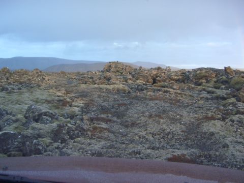 1974 Ford Bronco - A desolate landscape of rocks and moss stretches towards distant hills under an overcast sky.