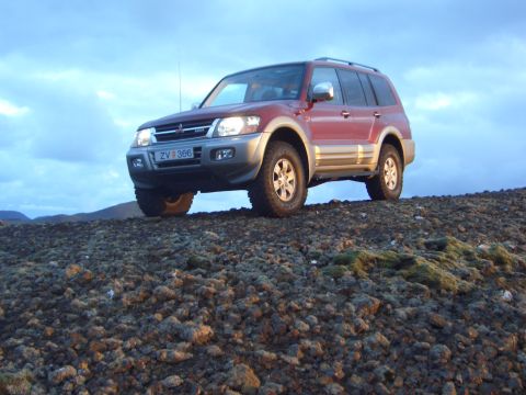 1974 Ford Bronco - This red SUV, identified by its license plate ZV 366, is parked on a rocky incline under a cloudy sky.