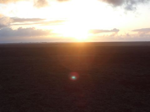 1974 Ford Bronco - The sun sets over a vast, dark field under a cloudy sky.