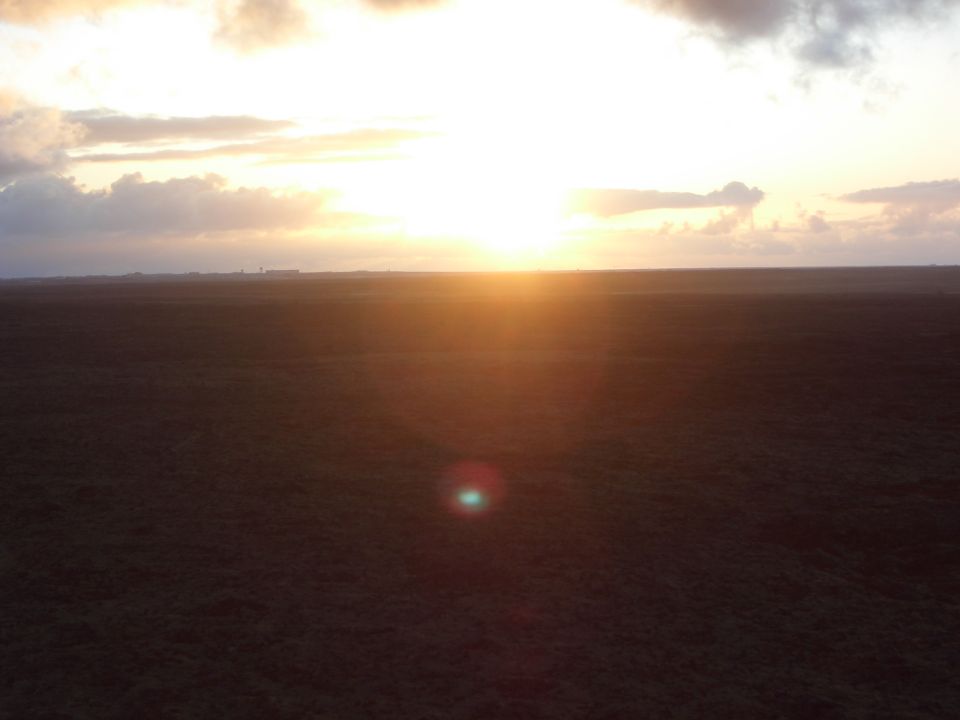 Sunset over a dark, grassy field with clouds