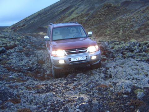 1974 Ford Bronco - A red SUV navigates a challenging, rocky landscape under a twilight sky.