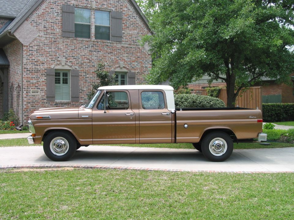 Brown 1970s Ford crew-cab long-bed pickup parked on a driveway by a brick house