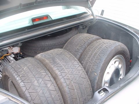 1987 Ford Mustang - Four spare tires and a car battery are stored in the trunk of a vehicle.