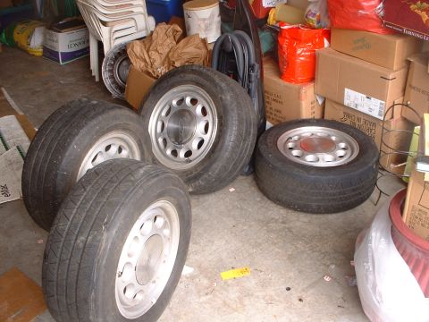 1987 Ford Mustang - Four tires and wheels are stored in a garage setting, surrounded by various items.