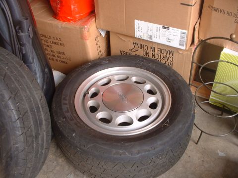 1987 Ford Mustang - A single Ford wheel and tire are shown in storage, surrounded by cardboard boxes and other tires.