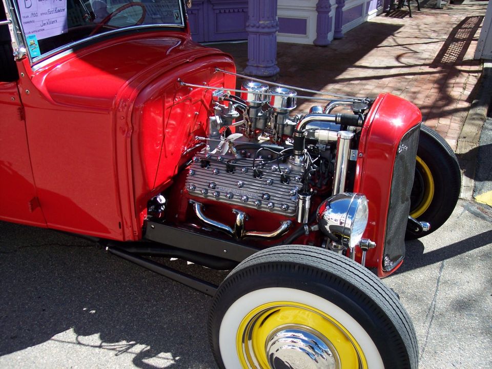 Red hot rod with yellow wheels and white wall tires, showing a V8 engine and chrome details