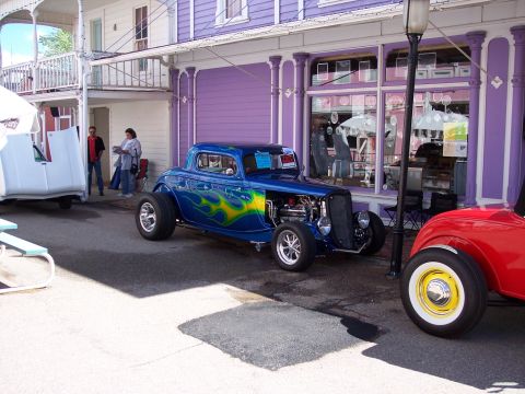 1972 Ford Ranchero - A blue custom hot rod with flame graphics is parked on a street next to a red car.