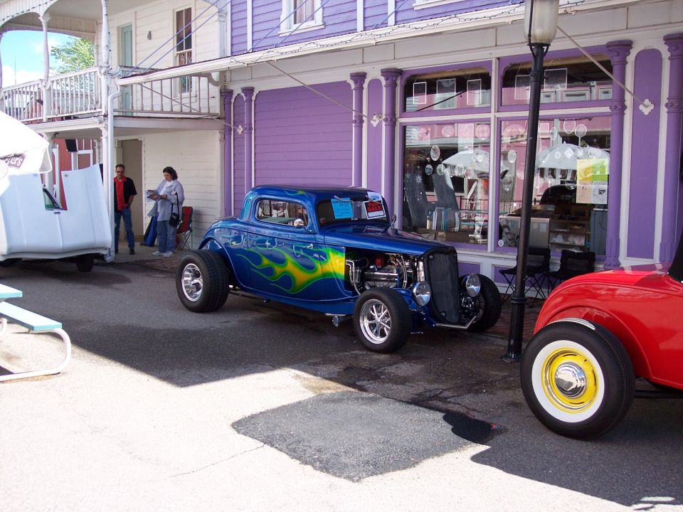 Blue custom hot rod with yellow and green flames parked on street next to a red car
