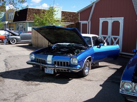 1972 Ford Ranchero - A blue 1970s Oldsmobile Cutlass is displayed with its hood and door open, parked near a red barn.