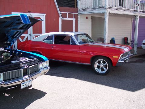 1972 Ford Ranchero - A red coupe with white racing stripes and a white roof is parked next to a blue car with its hood open.