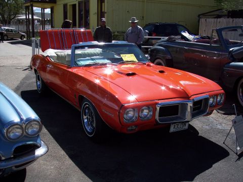 1972 Ford Ranchero - Orange 1969 Pontiac Firebird convertible with white interior and hood scoops, parked outdoors next to other vehicles.
