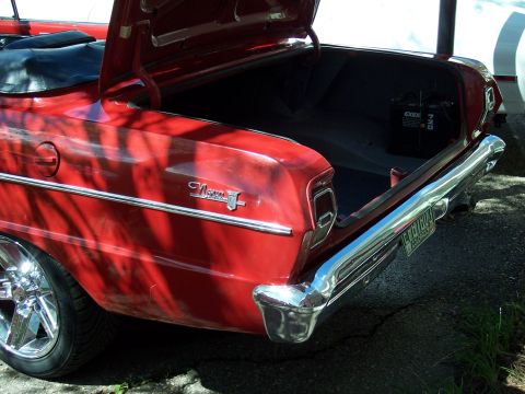 1972 Ford Ranchero - The rear of a red convertible is shown with its trunk open, revealing the battery and spare tire well.