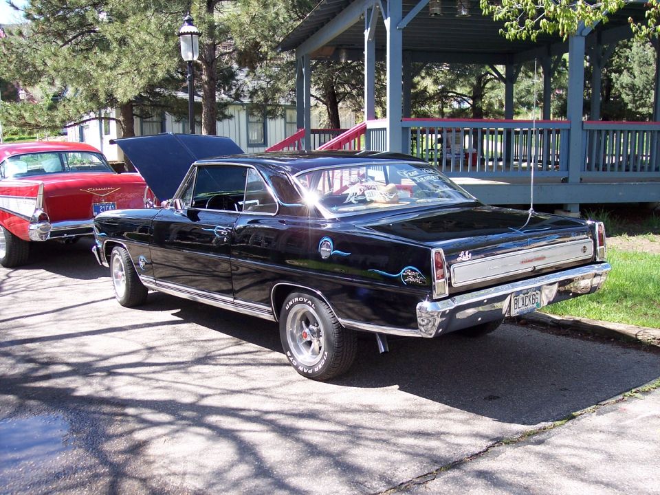 Black 1966 Nova parked next to a red 1957 Chevy. Hoods are up on both cars