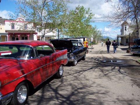 1972 Ford Ranchero - Two classic cars are parked on a street in front of old-fashioned buildings, with people walking in the background.