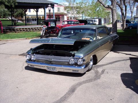 1972 Ford Ranchero - A vintage car is displayed with its hood up, revealing the engine bay, while other vehicles are parked nearby.