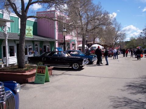 1972 Ford Ranchero - A street fair or car show is underway with vintage vehicles displayed outside businesses.