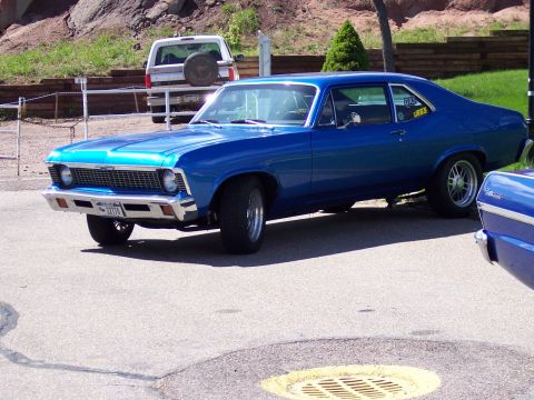 1972 Ford Ranchero - A bright blue coupe with a chrome grille and custom wheels is parked on a street. Another blue vehicle is partially visible in the foregrou…