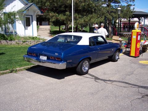 1972 Ford Ranchero - A blue coupe with a white roof is parked on asphalt, with a vintage gas pump and a gazebo in the background.