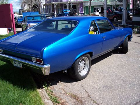 1972 Ford Ranchero - Blue coupe with racing stickers parked on a street, with other vehicles and buildings in the background.