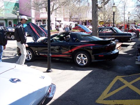 1972 Ford Ranchero - A black Pontiac Firebird Trans Am with red racing stripes is displayed at an outdoor car show.