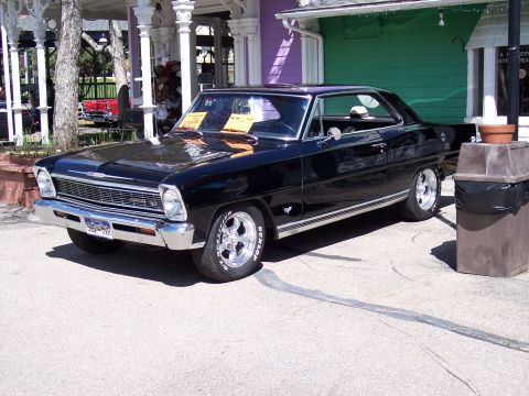 1972 Ford Ranchero - A classic black coupe sits parked on pavement in front of a colorful building, with a trash can nearby.