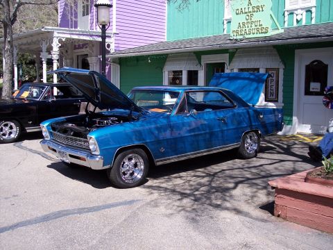 1972 Ford Ranchero - A blue 1966 Chevrolet Nova coupe is parked with its hood open, alongside a black car, in front of a building with colorful siding.