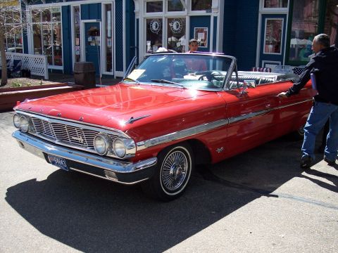 1972 Ford Ranchero - A bright red convertible with a white interior is parked on a street in front of a blue building.
