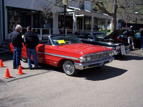 1972 Ford Ranchero - A red 1964 Ford Galaxie convertible is displayed alongside other vehicles, with people observing.