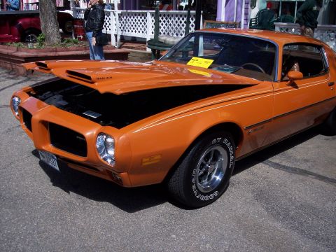 1972 Ford Ranchero - This orange muscle car, likely from the 1970s, features a Ram Air hood scoop and racing stripes.