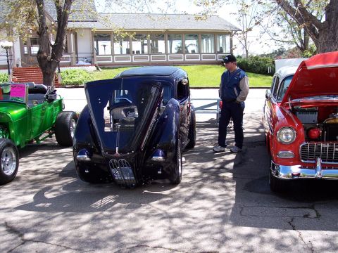 1972 Ford Ranchero - A dark blue hot rod is displayed with its hood open, parked alongside other vehicles at an outdoor event.