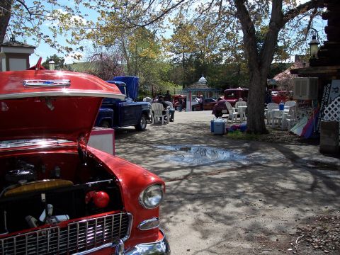 1972 Ford Ranchero - A red 1955 Chevrolet Bel Air with its hood open is parked in a lot with other vehicles and outdoor seating.