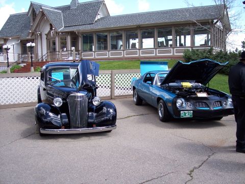 1972 Ford Ranchero - Two classic cars, a blue Camaro and a black vintage vehicle, are displayed outdoors with their hoods open.