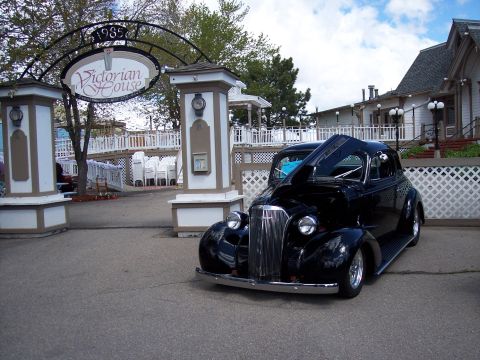 1972 Ford Ranchero - A black coupe is parked in front of the Victorian House entrance, with its hood open to reveal the engine.