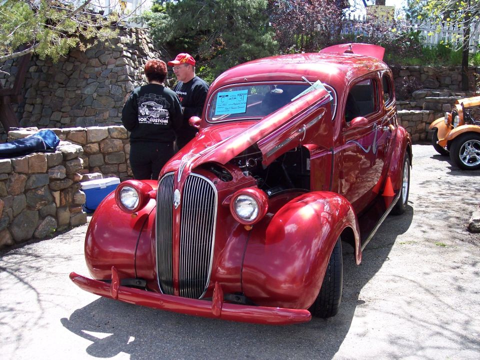 Red sedan with hood open, front view. Blue sign on windshield