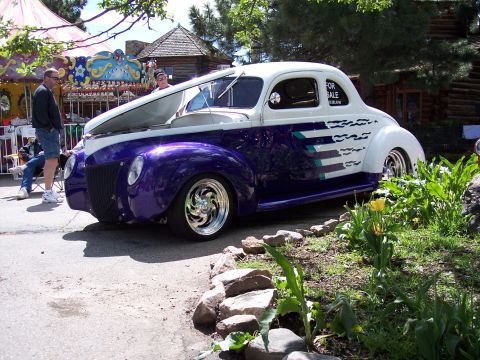 1972 Ford Ranchero - A two-tone custom coupe with purple fenders and a white body is parked near a carousel and a log cabin.