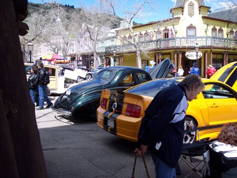 1972 Ford Ranchero - A yellow and black striped car is parked on a street with other vehicles and buildings in the background.