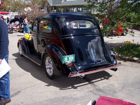1972 Ford Ranchero - A shiny black 1936 Ford Sedan hot rod is parked outdoors, reflecting the sky and surrounding trees.