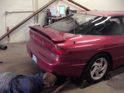 1989 Ford Probe - A person works on the underside of a red coupe in a garage setting.