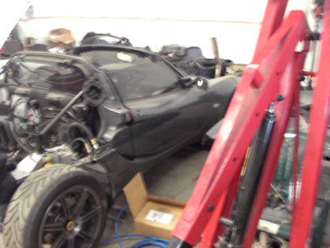 1989 Ford Probe - A dark sports car is partially disassembled in a workshop, with its engine compartment open and front wheel in view.