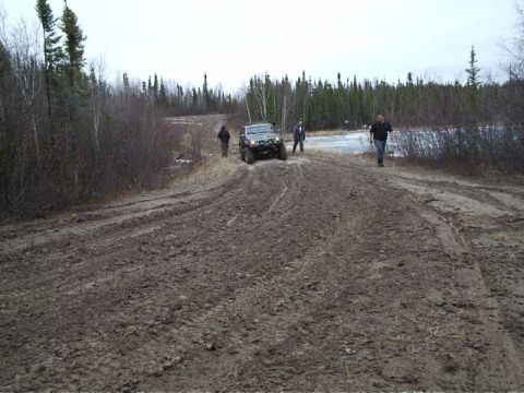 1986 Ford F-150 - An off-road vehicle struggles on a muddy trail with several people nearby.