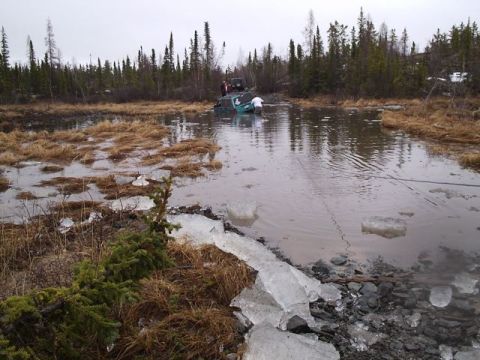 1986 Ford F-150 - A vehicle is stuck in a body of water with people attempting to free it.