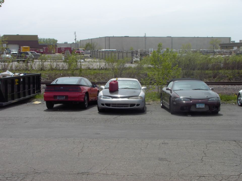 Three coupes parked side-by-side, one red, one silver with a red gas can on the hood, and one dark purple convertible