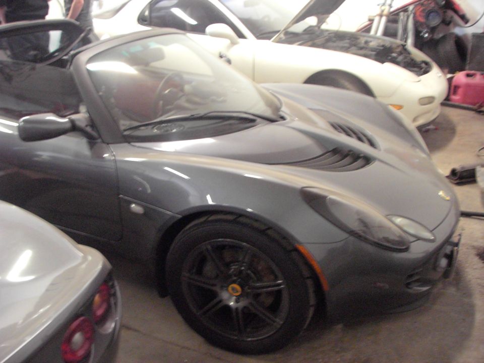 Gray convertible sports car with black wheels and side vents. Other cars visible