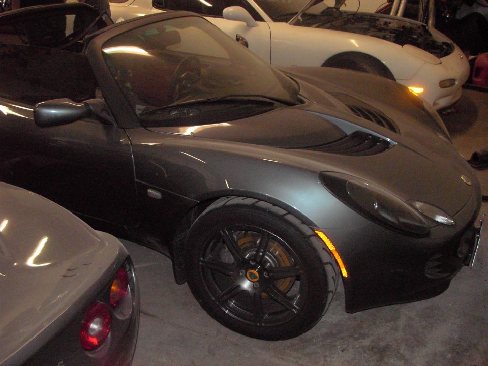 Dark grey convertible sports car parked next to a white car with hood open