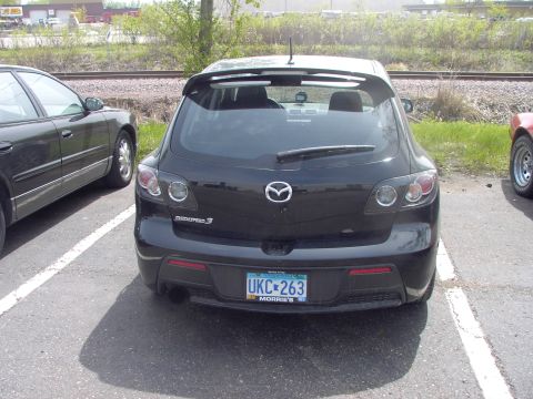 1989 Ford Probe - A black Mazda 3 hatchback is parked in a lot, showing its rear end and license plate.