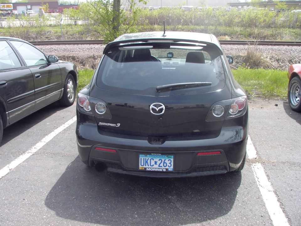 Black Mazda 3 hatchback rear view, parked outdoors with a spoiler and a license plate reading UKC 263
