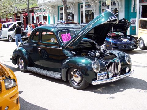 1972 Ford Ranchero - A dark green coupe from the 1940s is displayed with its hood open, parked on a street with other vehicles.