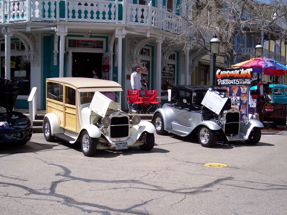 Two vintage Ford Model A style cars parked on street, one a woodie wagon, the other a coupe with flames