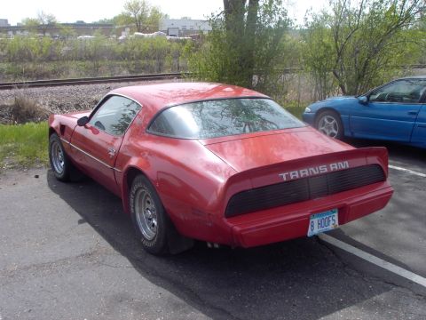 1989 Ford Probe - This red Pontiac Trans Am is seen from the rear, its distinctive badging and a blue car parked nearby.