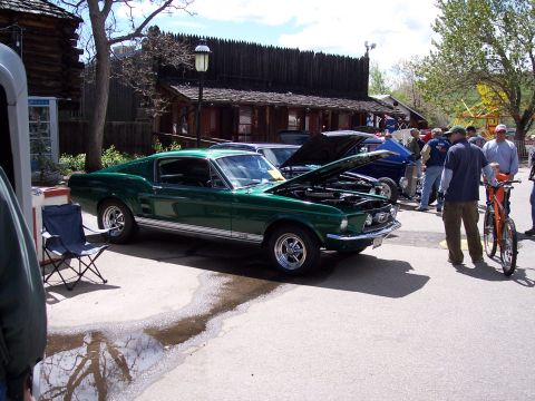 1972 Ford Ranchero - A classic green Mustang is displayed with its hood up, alongside other vehicles and people at an outdoor event.